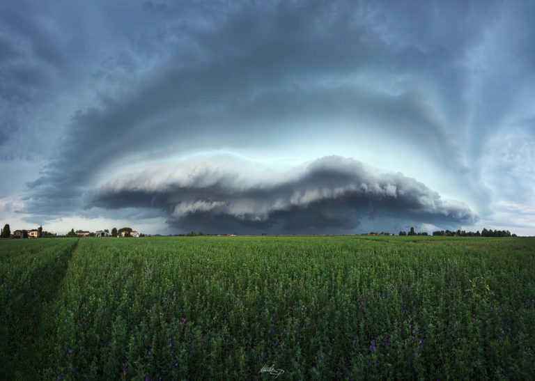 Nube arcuata sull’orizzonte: dramma di luce tra i campi